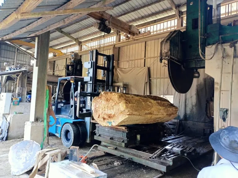 Skilled craftsman using industrial equipment to polish and finish a large, unique petrified wood slab in an Indonesian workshop.