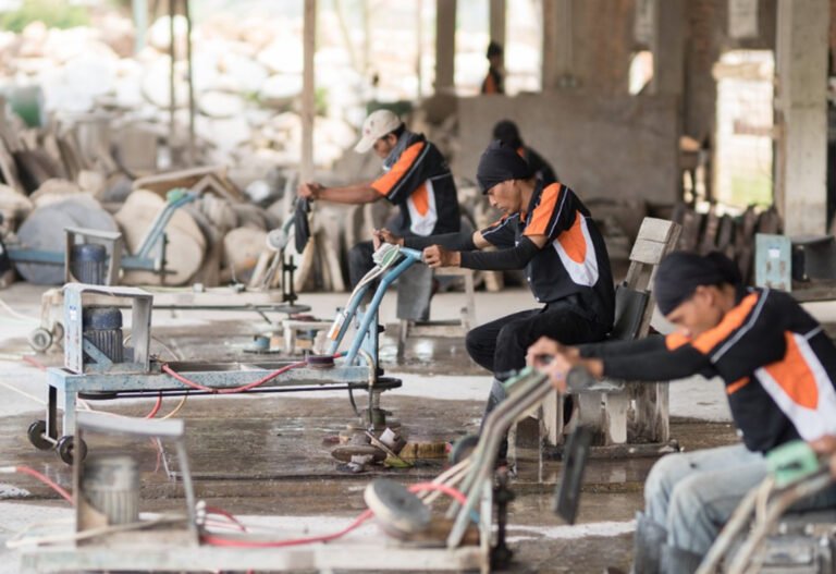 Skilled Indonesian artisan polishing a large, colorful petrified wood slab with industrial equipment in a professional workshop.